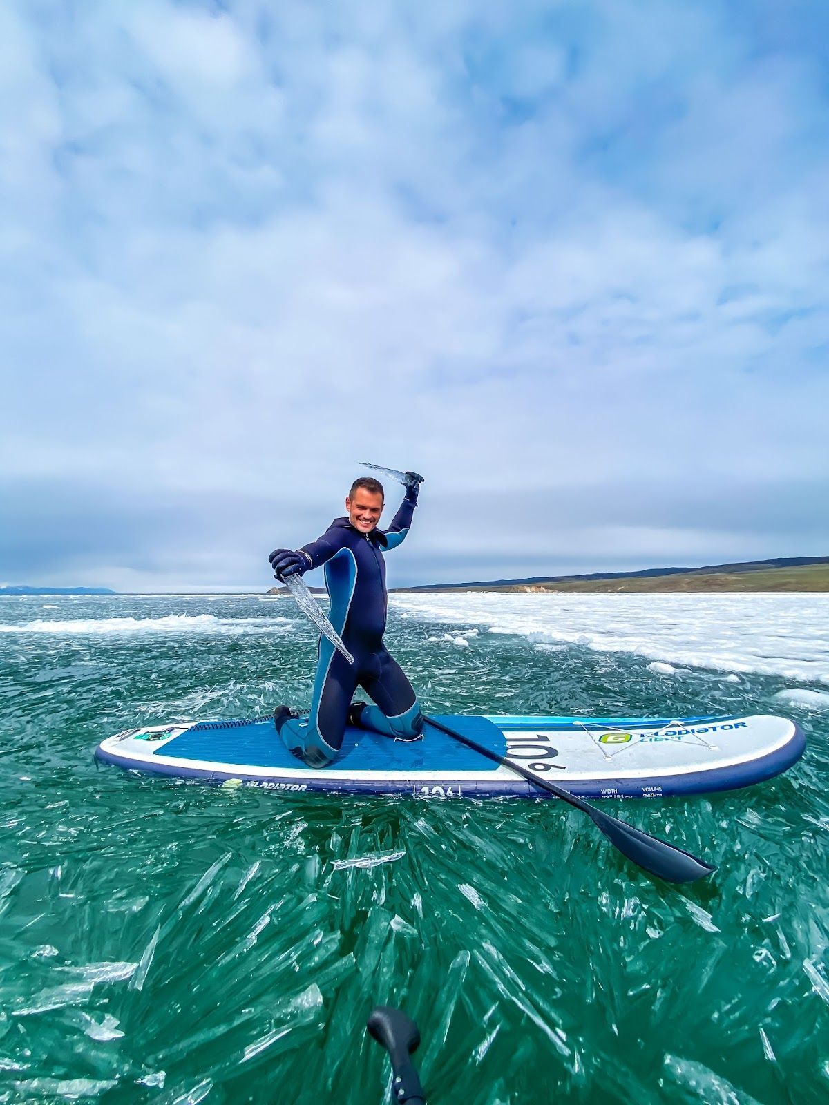 Человек в гидрокостюме на САПе посреди озера