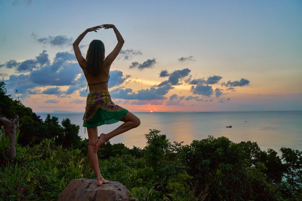 Девушка занимается йогой с видом на закат